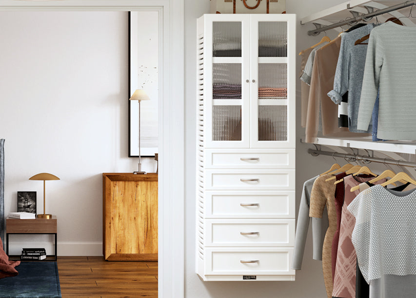white storage tower with shelves and drawers and doors in master bedroom closet with clothes hanging